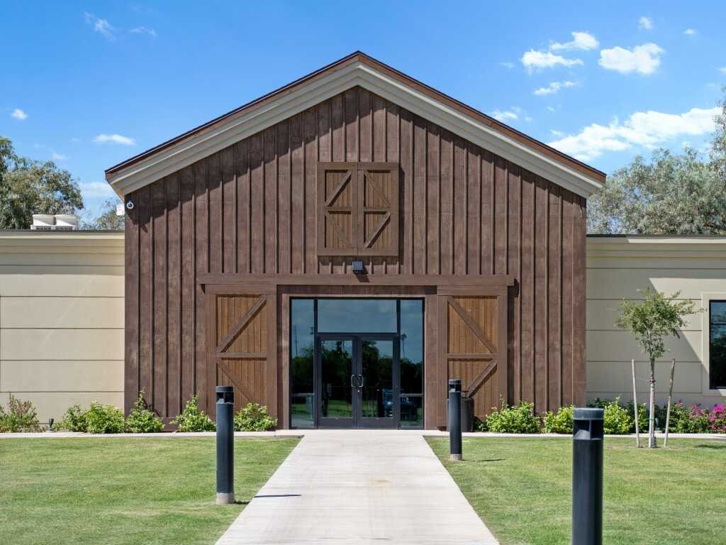 A light-colored building with a dark, barn-style wooden entrance and a central glass door under a triangular roof.