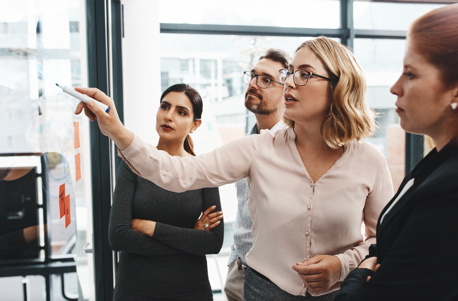 A woman is pointing at a whiteboard while a group of people look on.