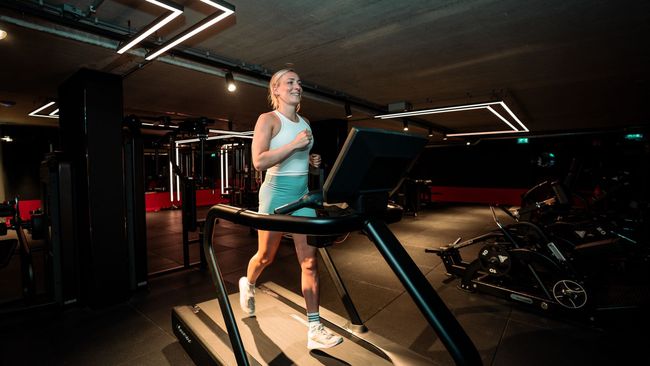 Een persoon in sportkleding tilt een halter boven zijn hoofd in een sportschool.