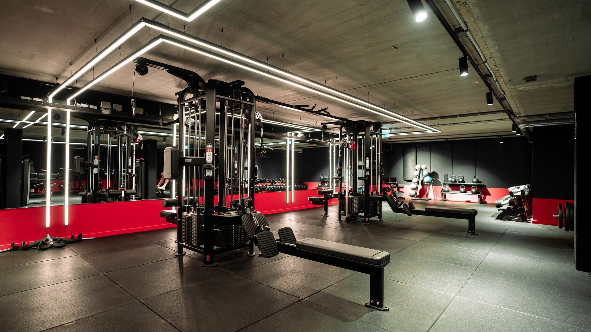Een rij zwarte dumbbells in een schemerig verlichte sportschool met blauwe lampen en een wazig persoon op de achtergrond.