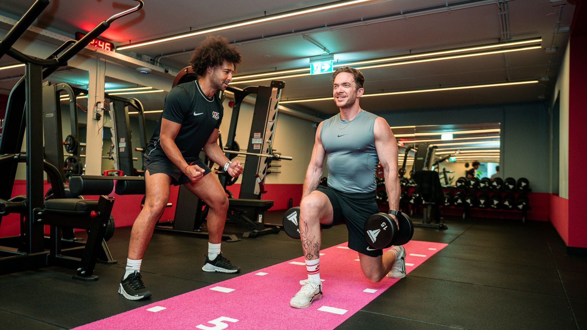 Een trainer helpt iemand bij het gebruik van een kabelmachine in een sportschool.