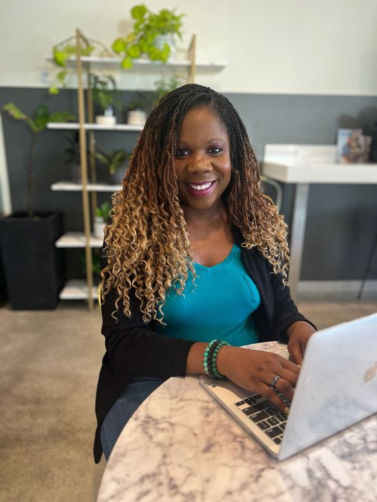A woman is sitting at a desk with a laptop and a vase of flowers.