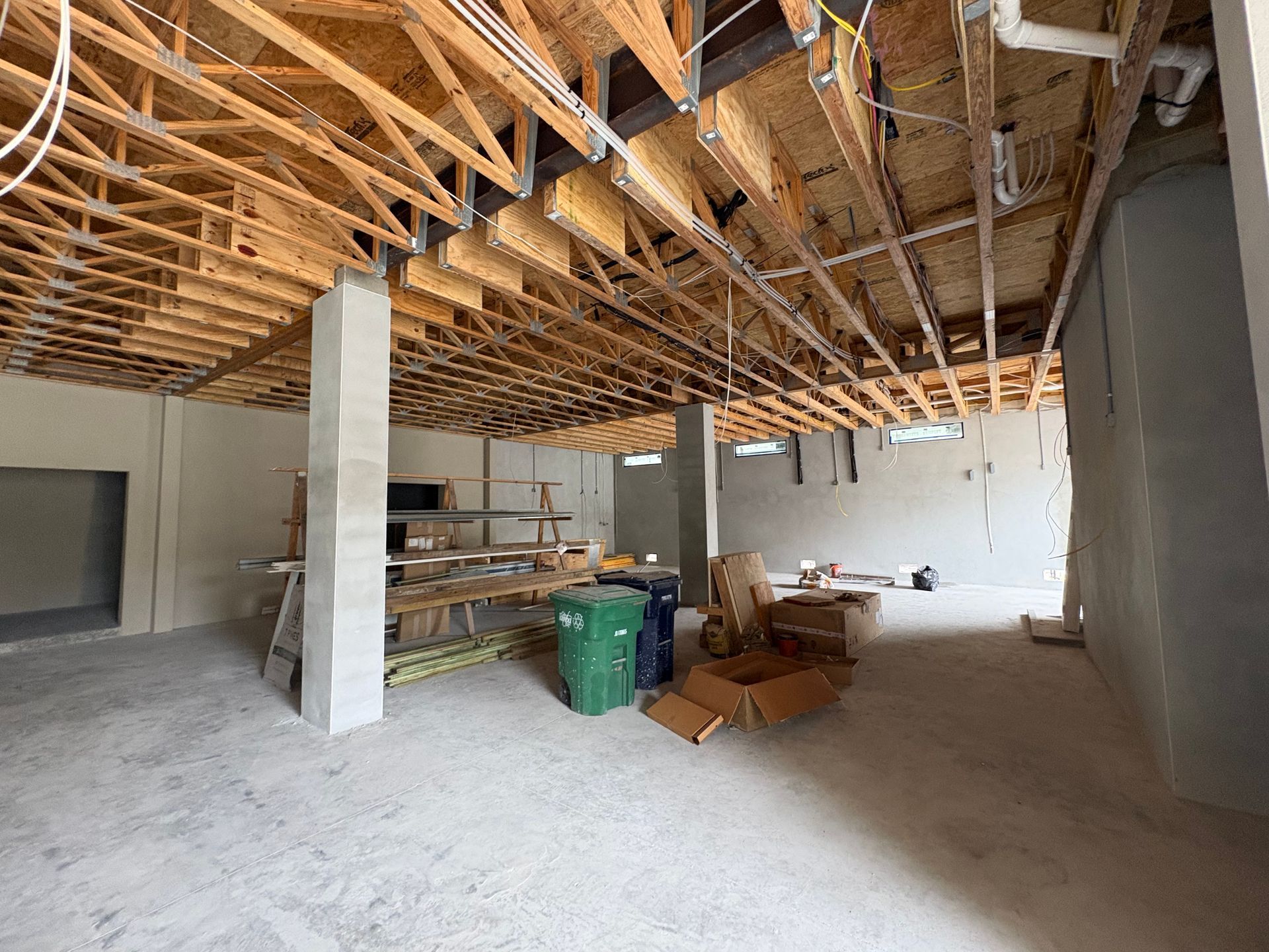 Unfinished interior with exposed wooden ceiling beams, concrete floor, and construction materials scattered around.