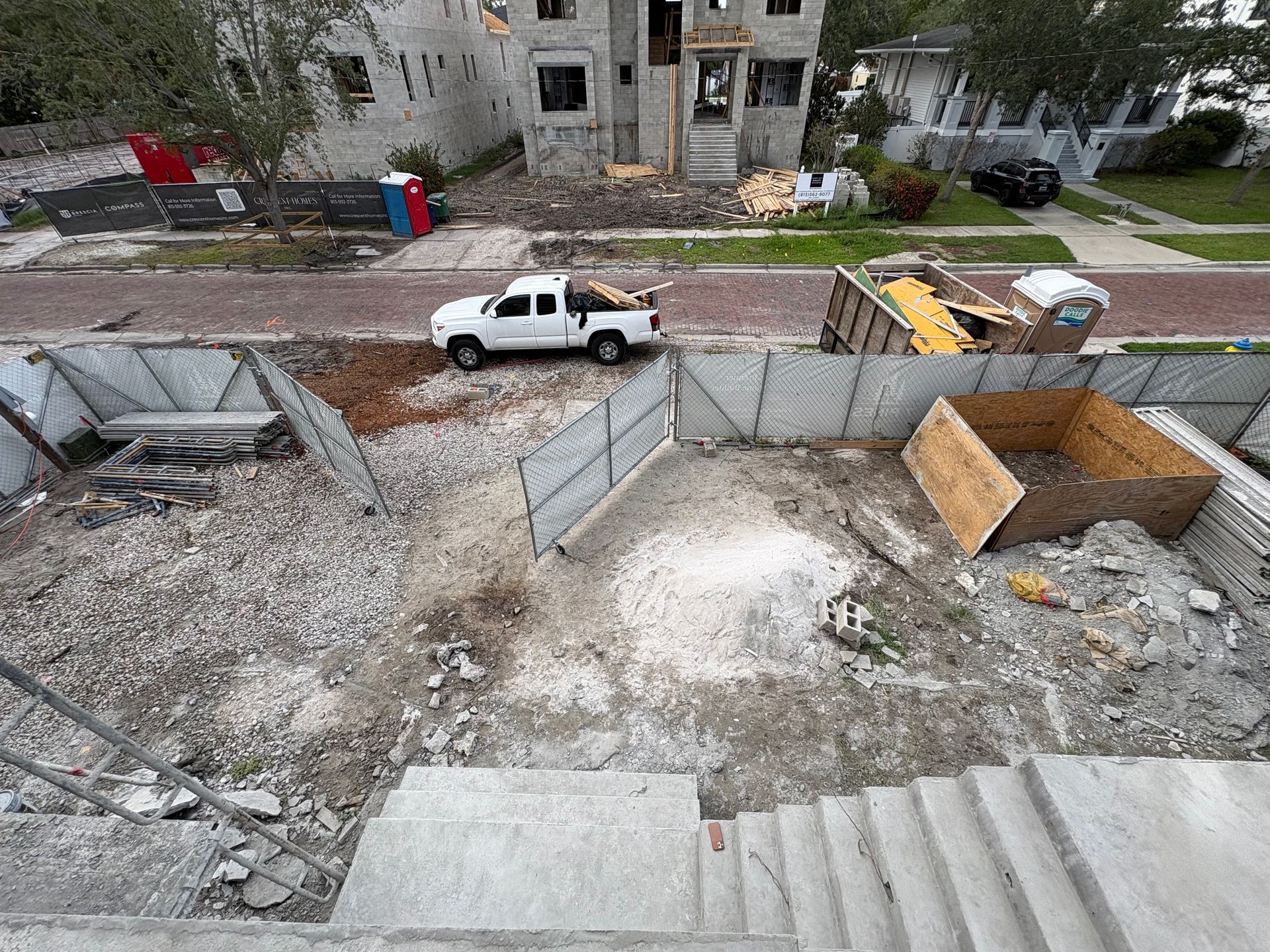 Construction site with debris, a white pickup truck, and stone stairs beside apartment buildings