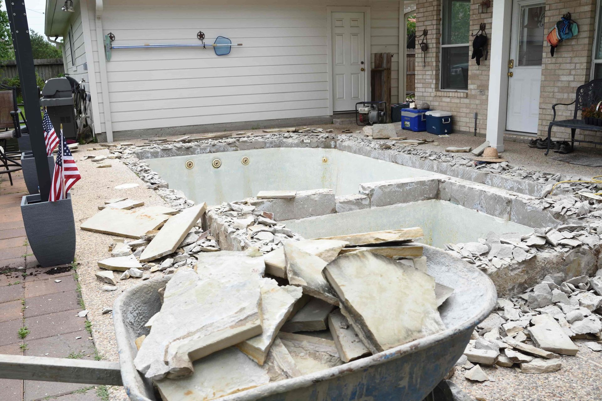 Demolished backyard pool with rubble and debris beside a house and garage