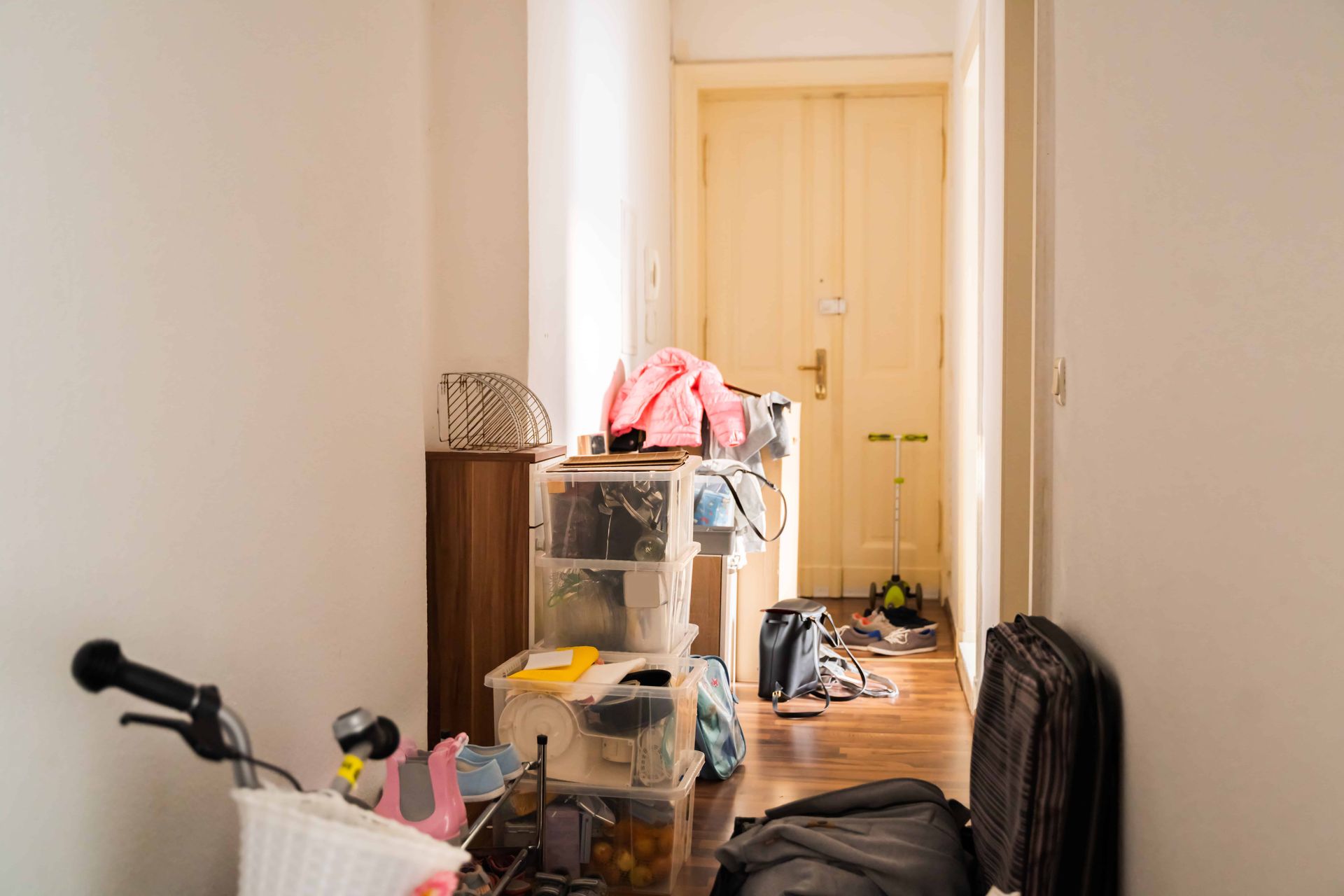 Cluttered hallway with boxes, luggage, and a bicycle in front of a closed door.