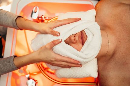 A person receives a warm towel treatment on their face during a spa service in a salon bowl.