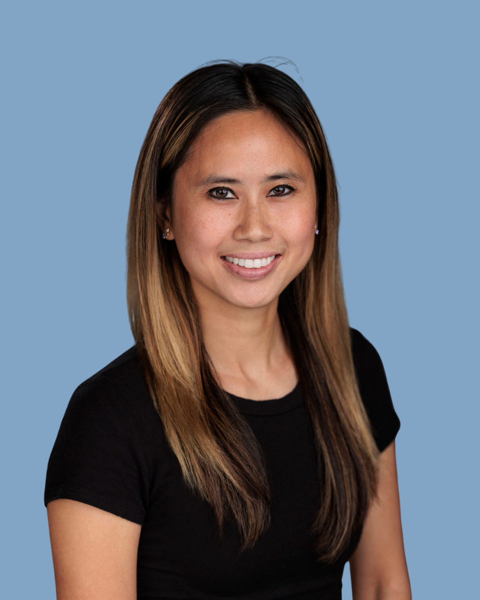 Smiling person with long dark hair in a black shirt against a teal background