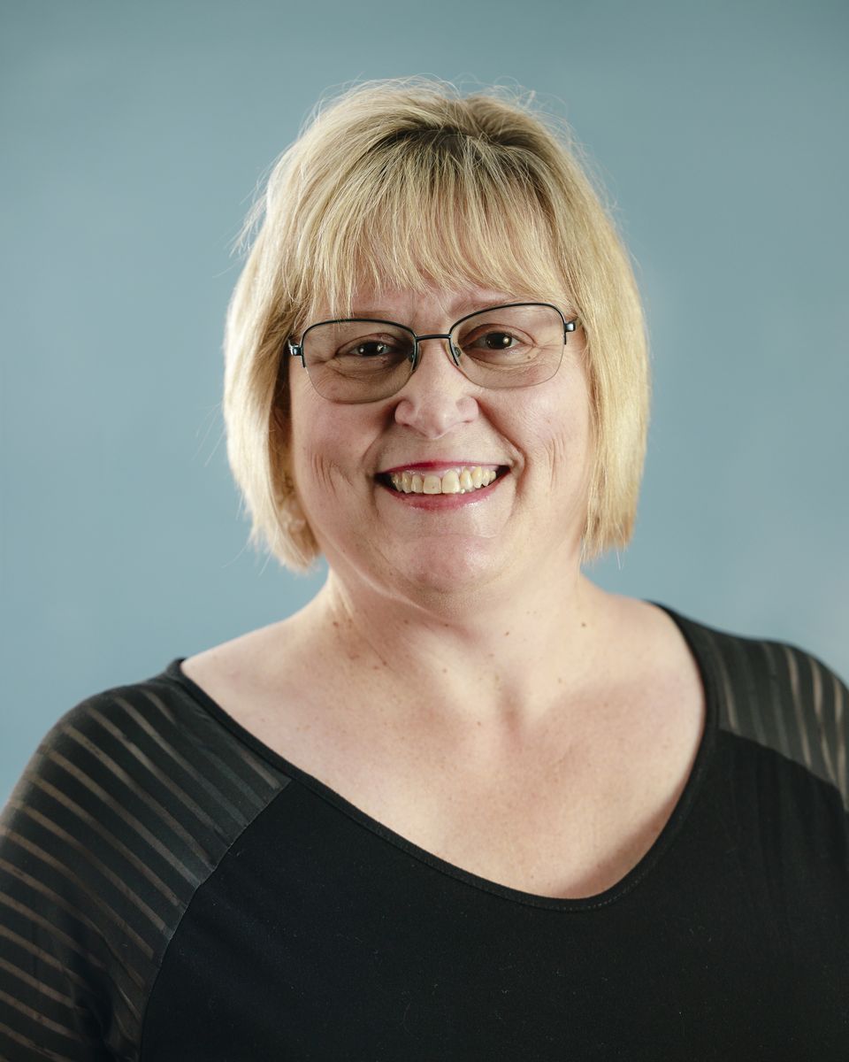 Smiling person with long dark hair in a black shirt against a teal background