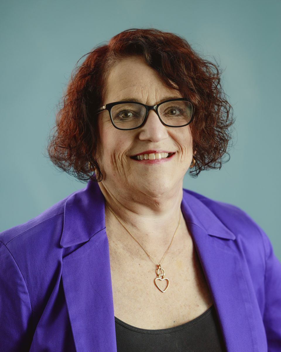 Smiling person with long dark hair in a black shirt against a teal background