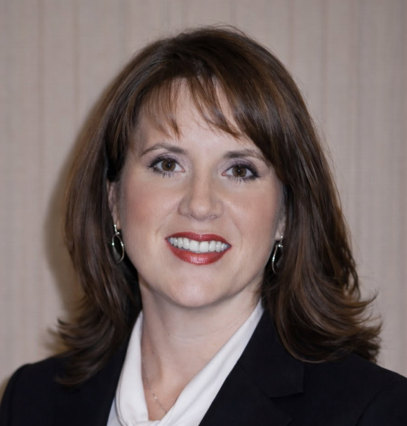 Woman with brown hair smiling, wearing a dark blazer and white shirt.