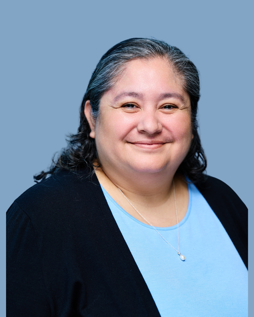 Smiling person with long dark hair in a black shirt against a teal background