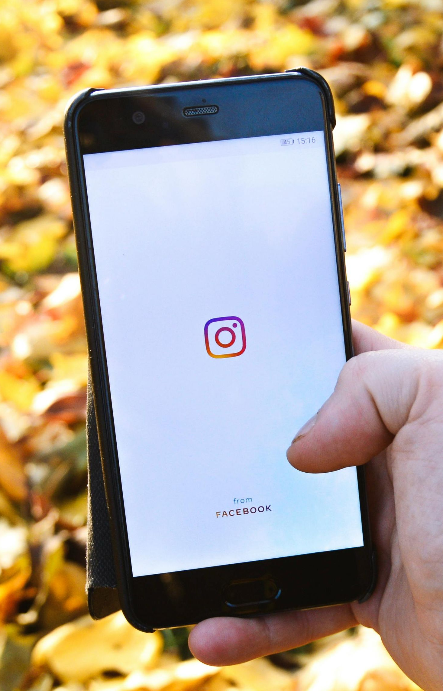 Hand holding a smartphone showing the Instagram logo on a white screen outdoors.