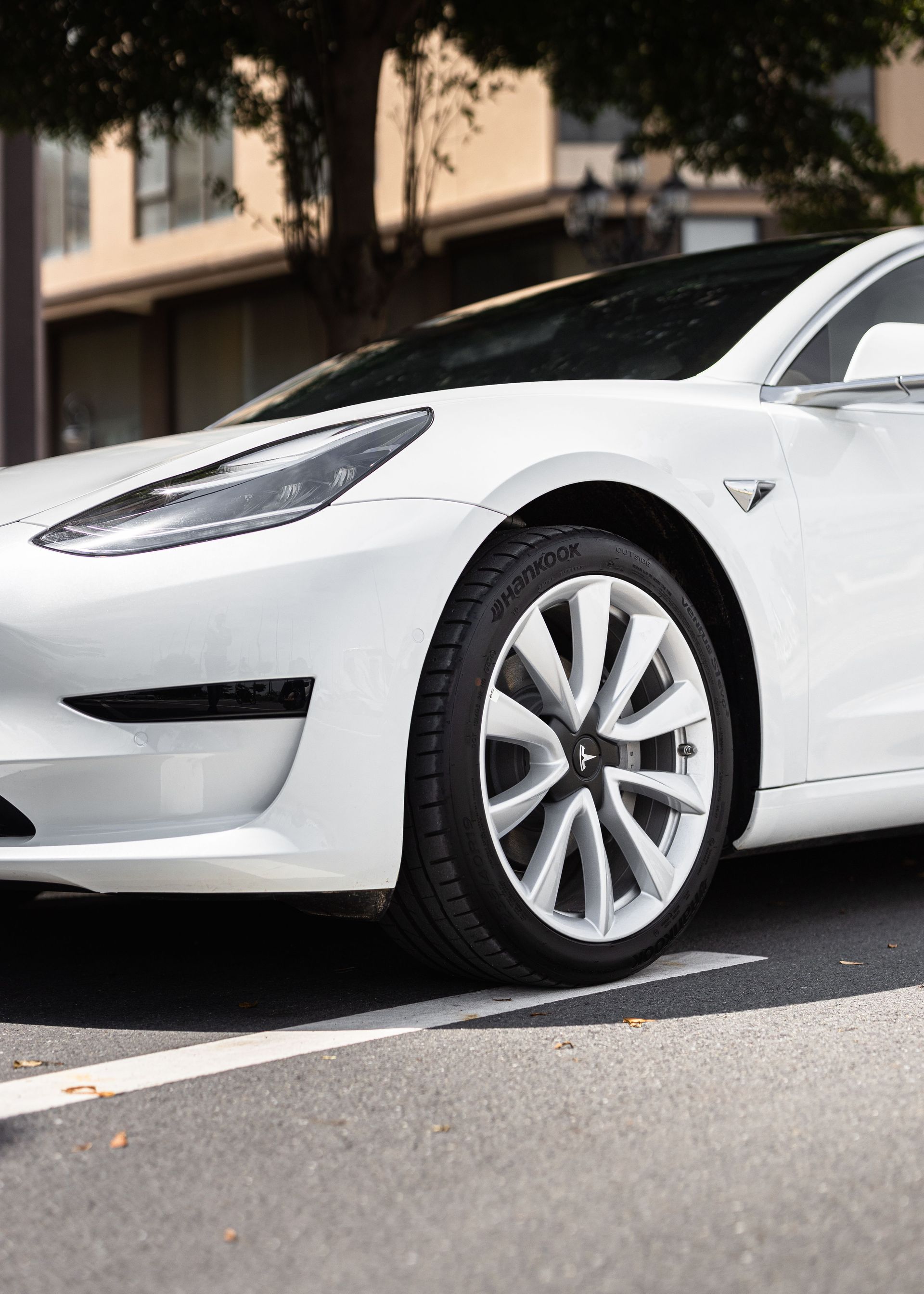 White electric sedan parked on a city street, front wheel and headlight visible.