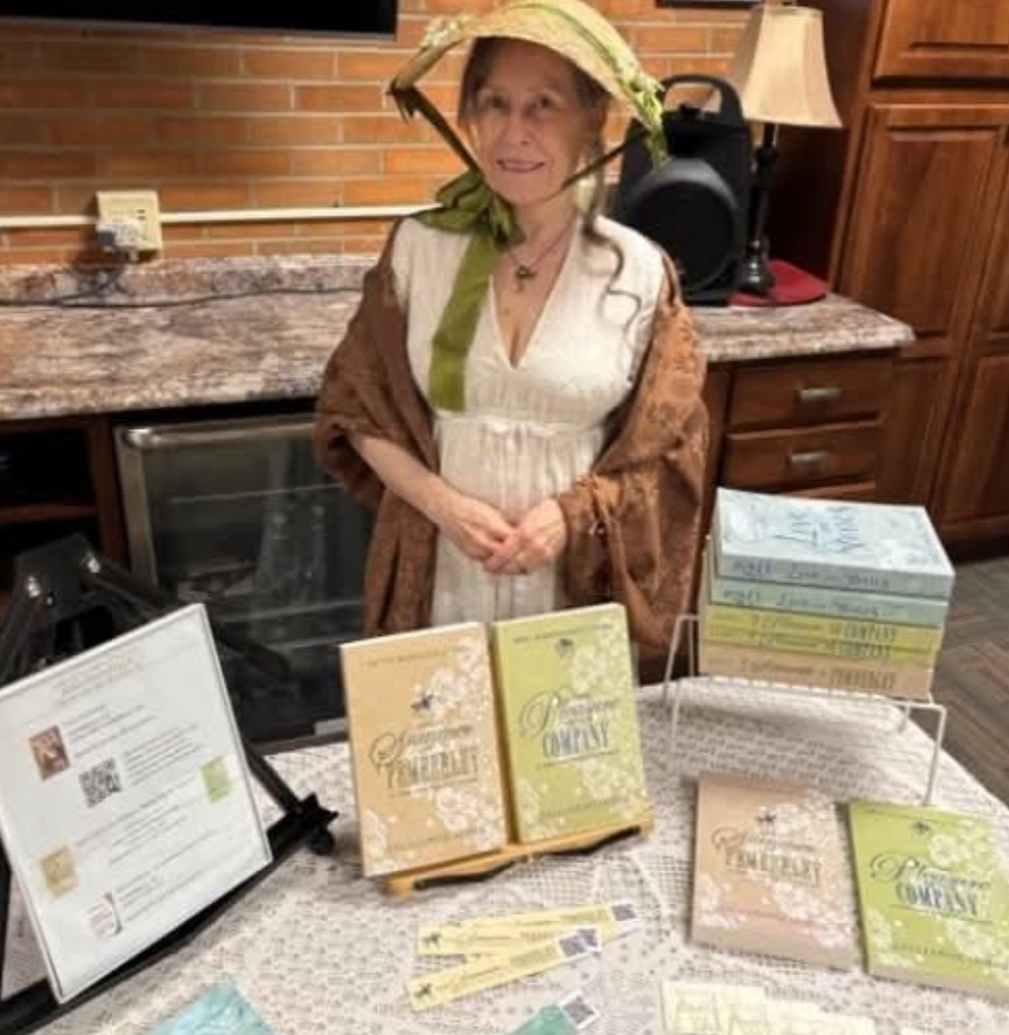 A person in 19th-century attire stands behind a table displaying copies of the book