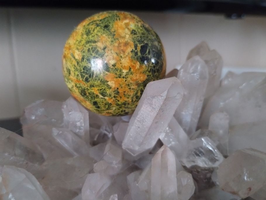 Yellow and green patterned sphere sits on a cluster of clear quartz crystals.