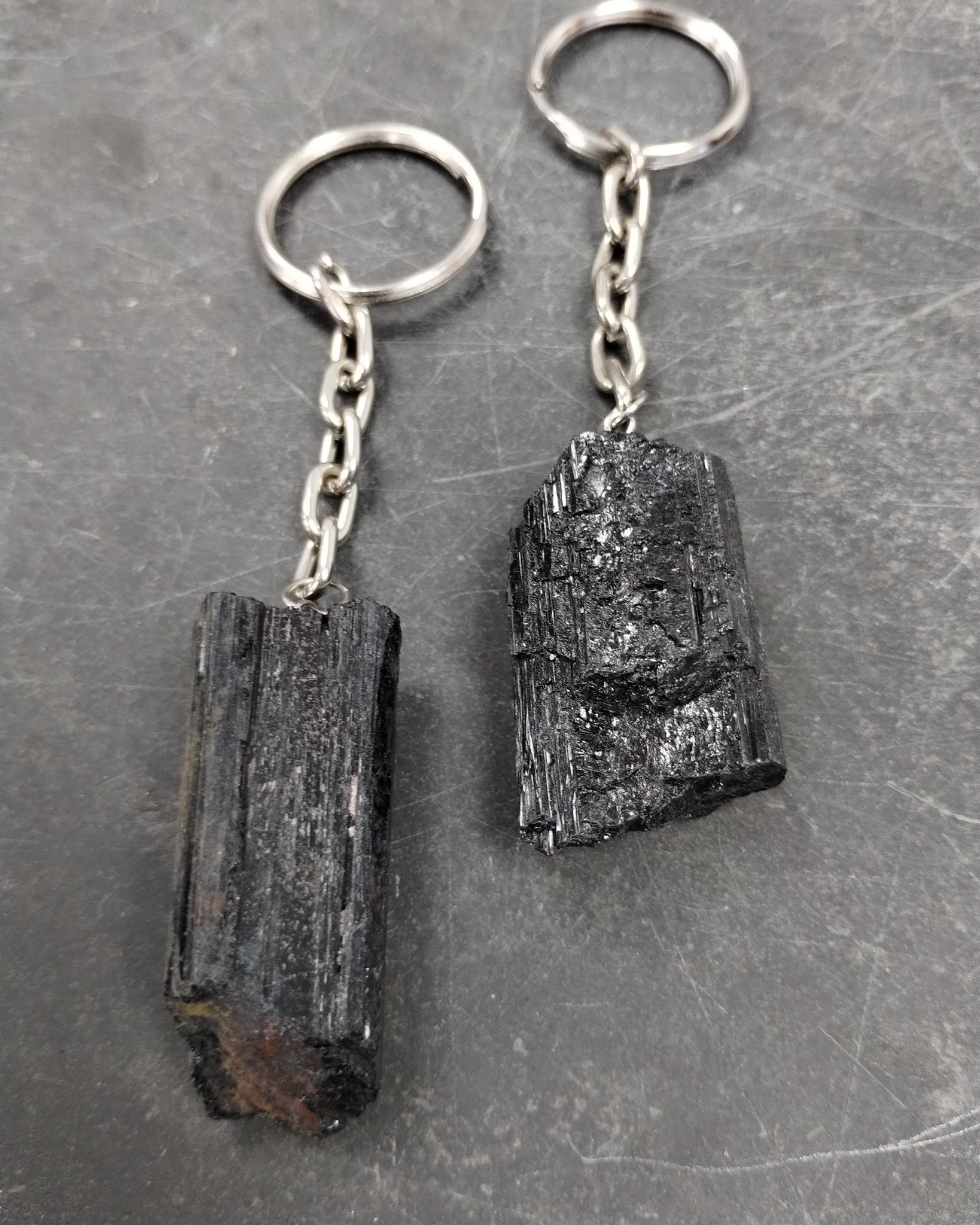 Two black tourmaline crystal keychains on a gray surface. Each has a silver chain and ring.