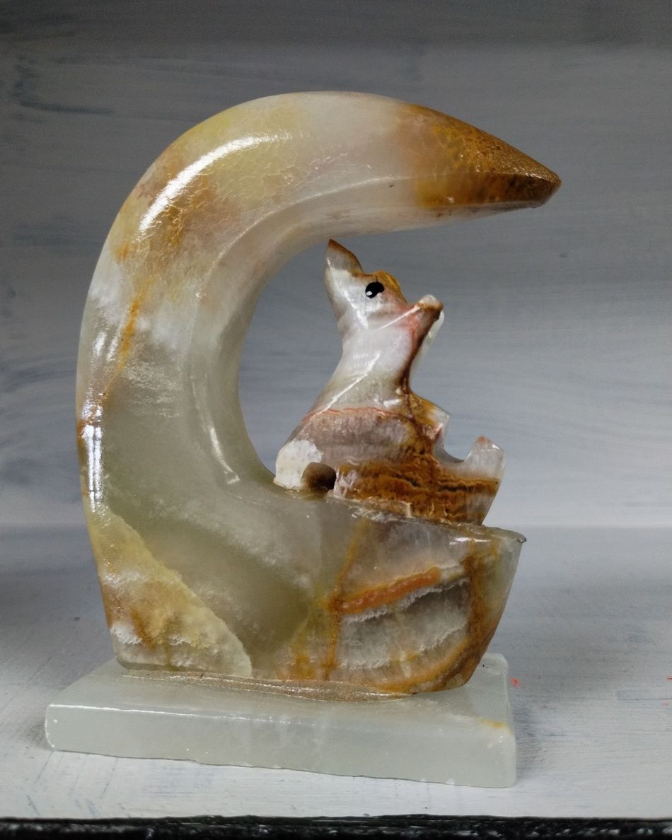 Stone sculpture of a small animal, possibly a fox, gazing upward. Set beneath a curved onyx formation.