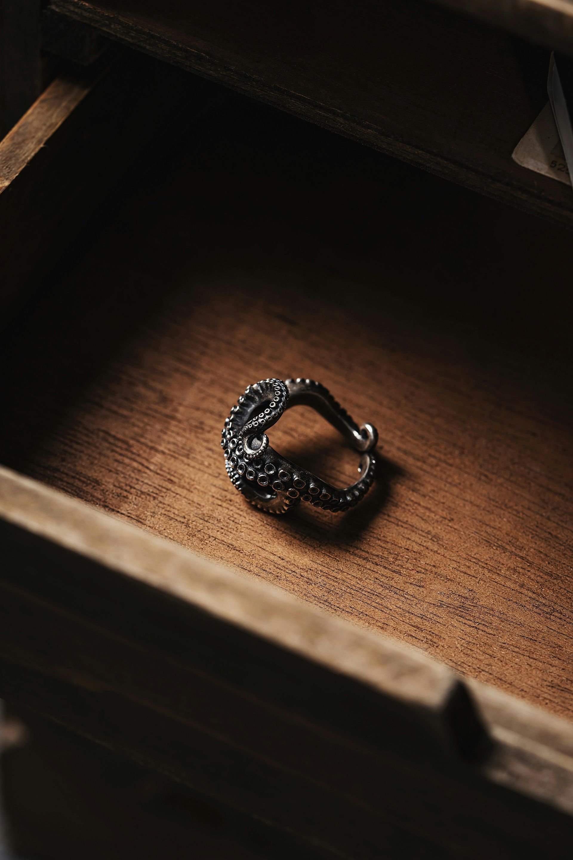 Silver ring, possibly dragon-themed, inside a wooden drawer.
