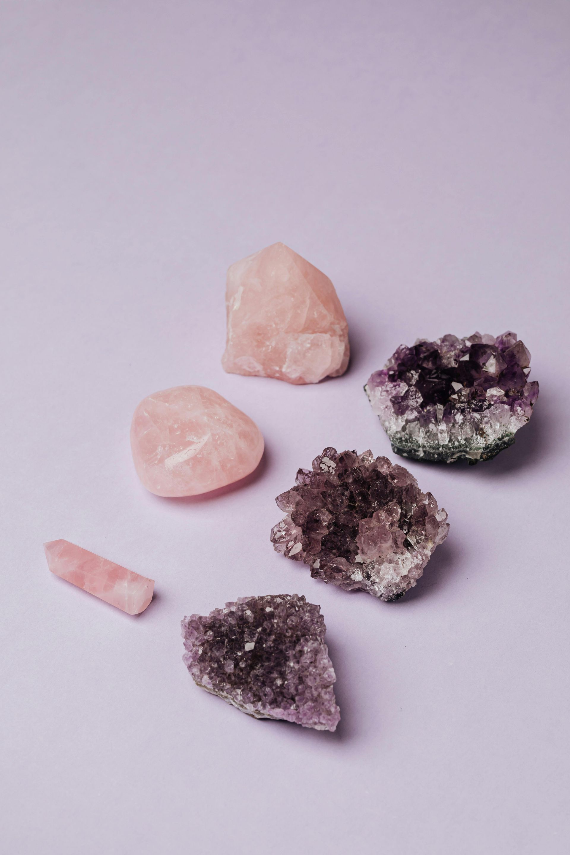 Assorted rose quartz and amethyst crystals on a lavender surface.