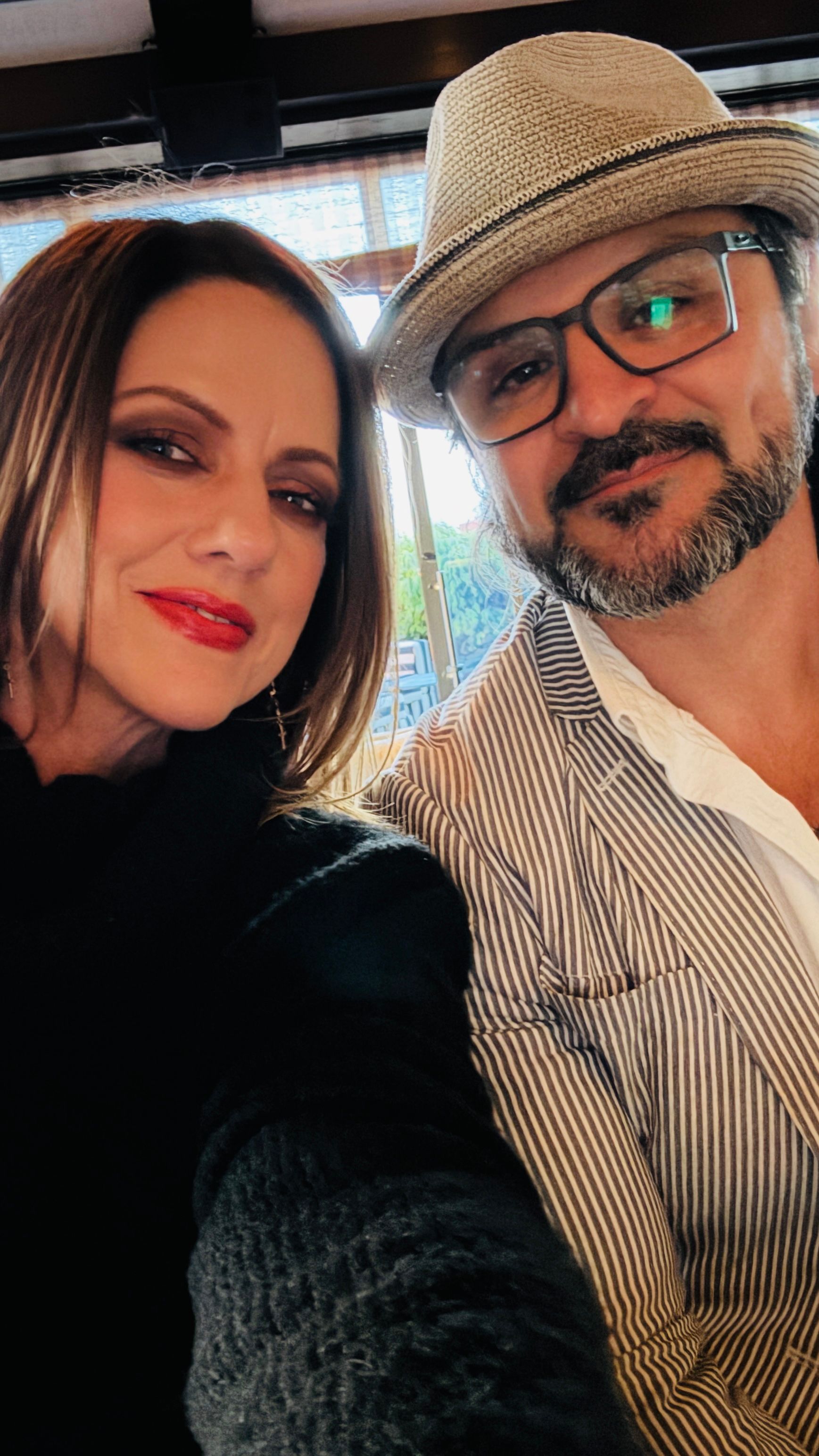 A man and a woman are posing for a picture together . the man is wearing a hat and glasses.
