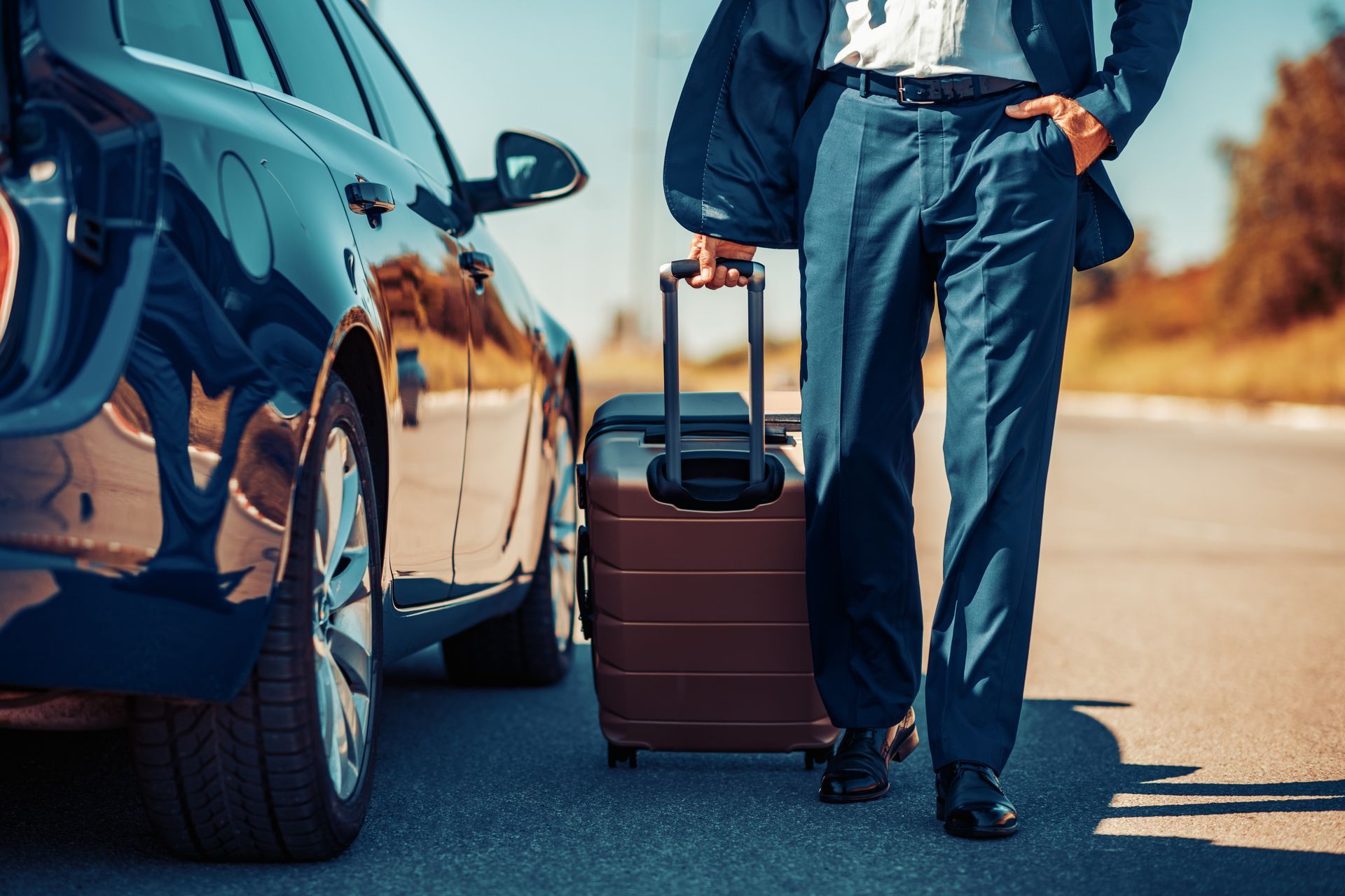 a man in a suit is standing next to a car with a suitcase .