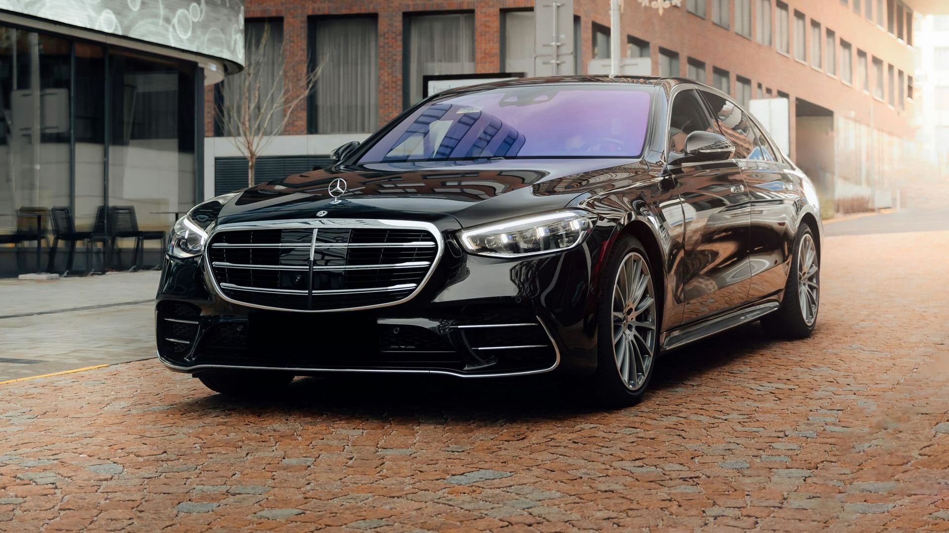 A black mercedes benz s class is parked on a cobblestone street in front of a building.