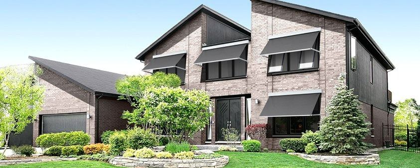 A Large Brick House With Black Awnings on the Windows — Simply Smarter Blinds in North Arm Cove, NSW