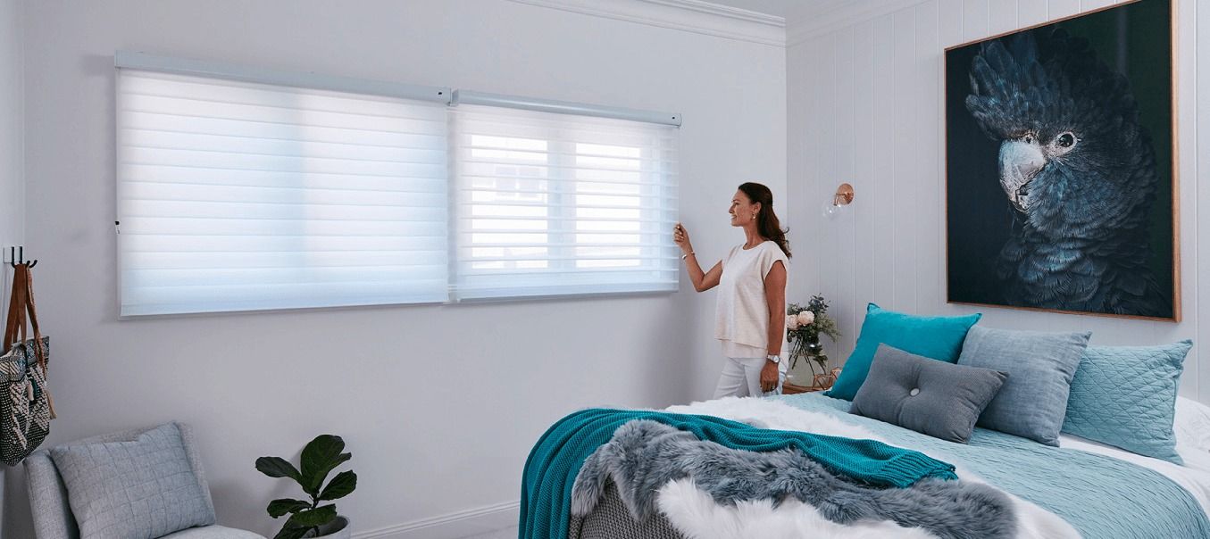 A Woman is Standing in a Bedroom Next to a Bed — Simply Smarter Blinds in Tea Gardens, NSW