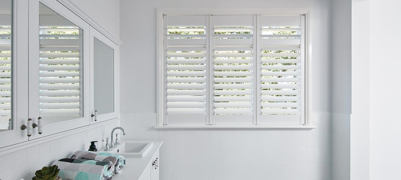 A Bathroom With a Sink, Mirror and Shutters on the Window — Simply Smarter Blinds in Tea Gardens, NSW
