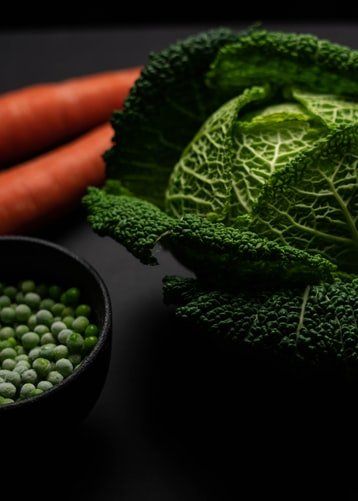 Un bol de petits pois et de carottes à côté d'un chou sur une table.
