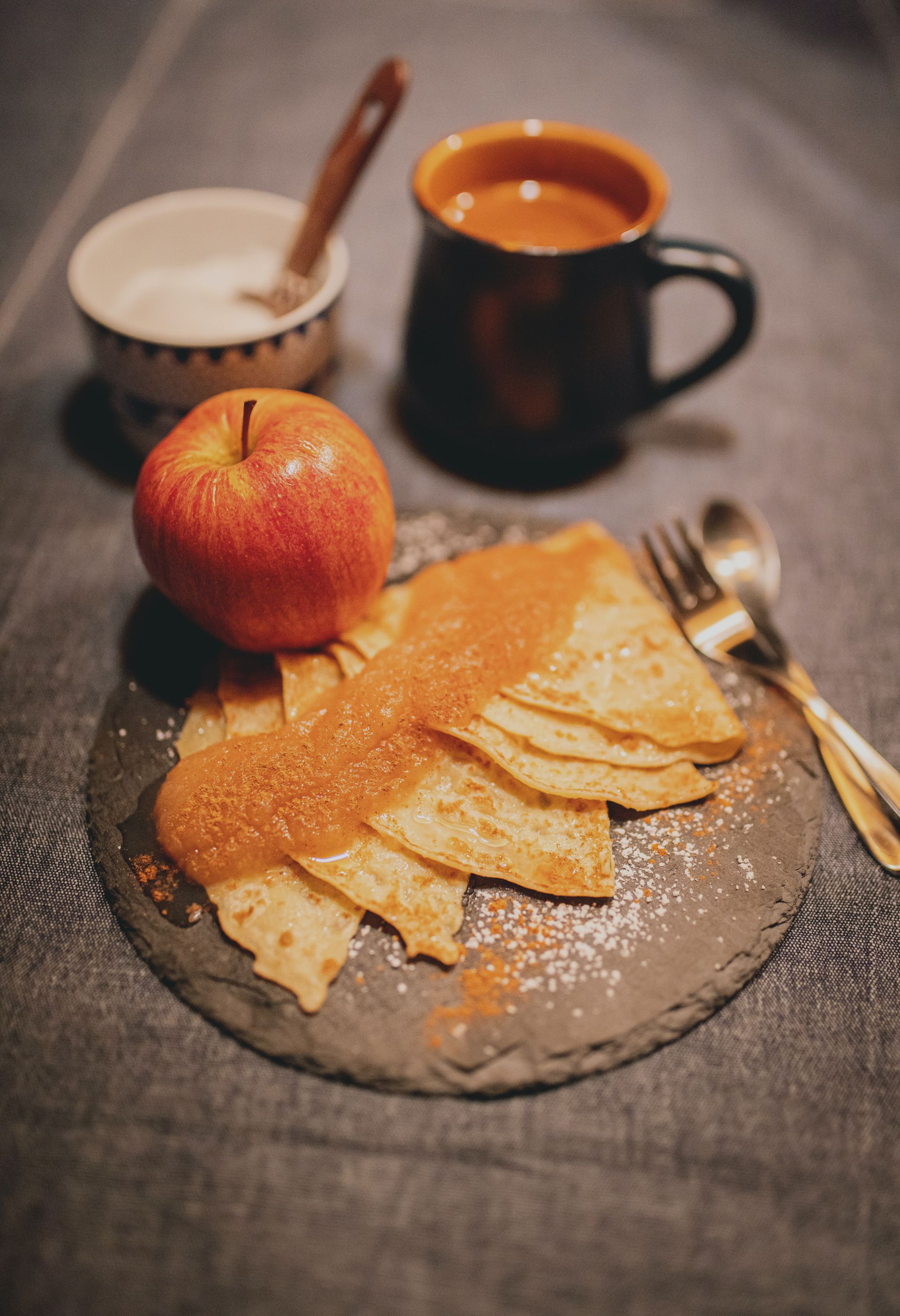Un gros plan d'une assiette de nourriture avec une crêpe, une pomme et une tasse de café sur une table.