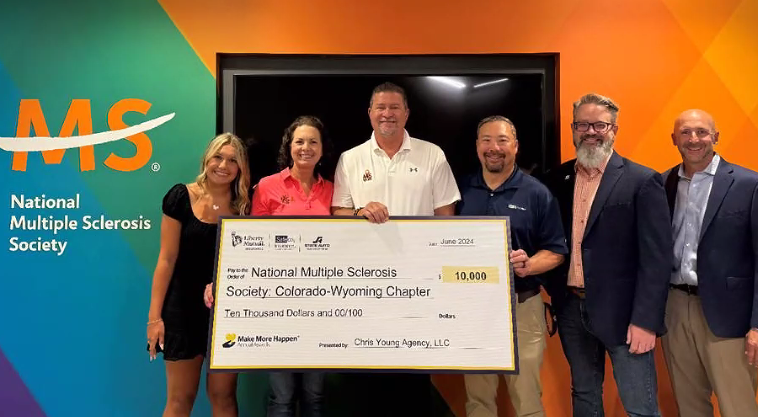 Group holding a large check for the National Multiple Sclerosis Society. Orange wall with MS logo.