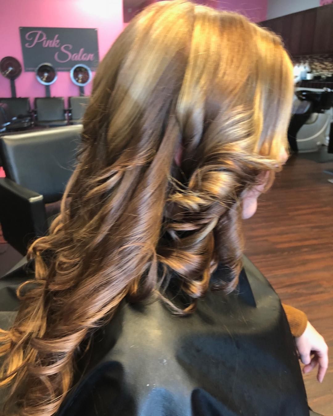 Long, curled auburn hairstyle shown from the back in a salon chair