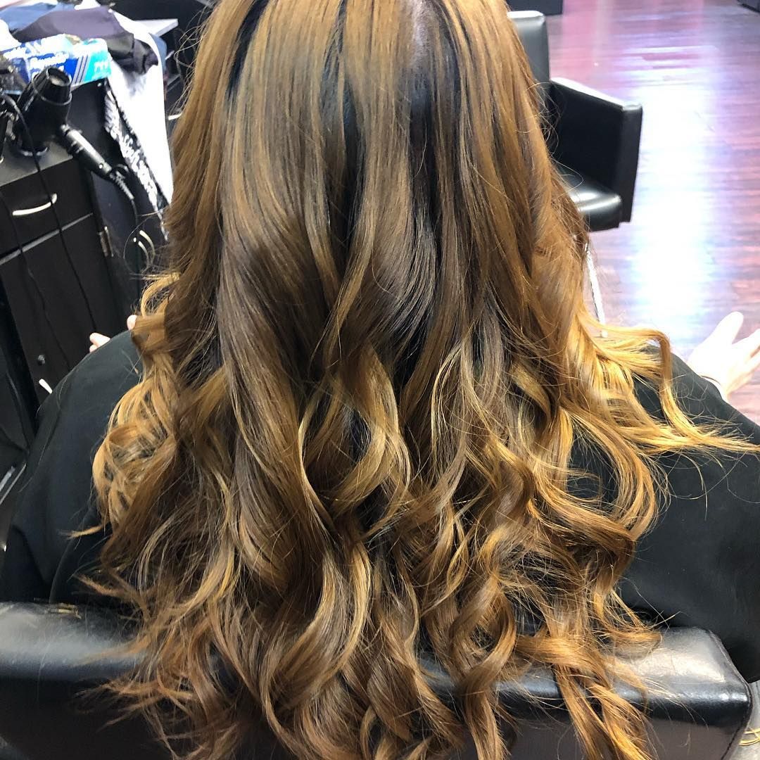 Long wavy brown hair with blonde highlights, viewed from behind in a salon chair