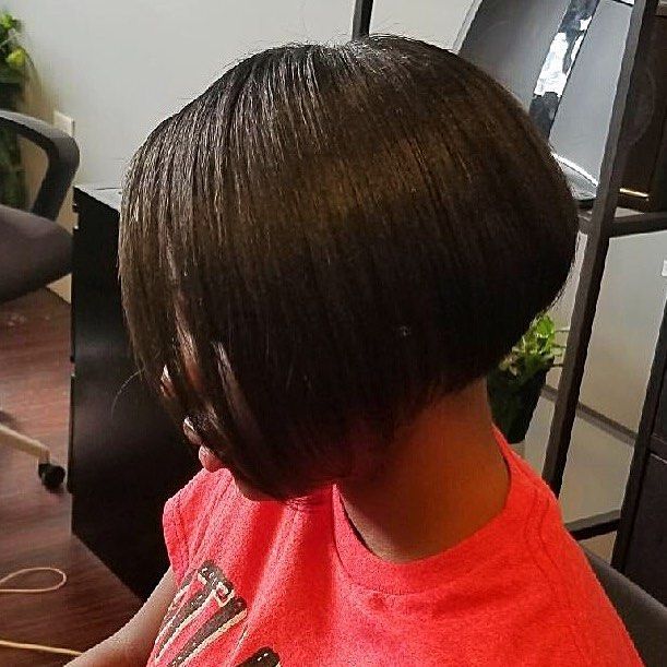 Side profile of a person with a short dark bob haircut wearing a red shirt indoors
