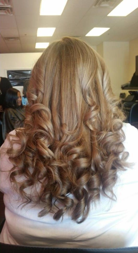 Curly light brown hair styled in loose curls, viewed from behind in a salon chair.
