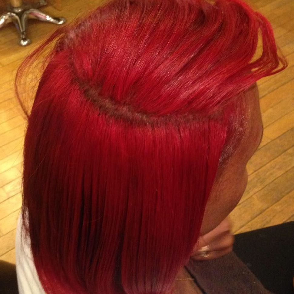 Bright red styled hair with a smooth side part and long straight strands in a salon setting