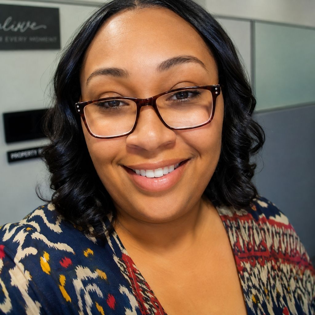Smiling woman wearing glasses in a patterned sweater, indoors with a blurred office background