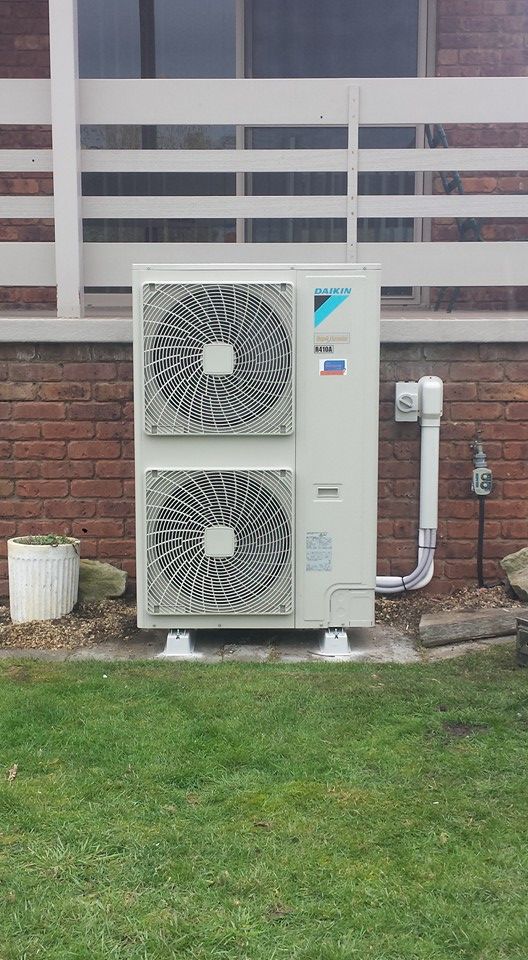 A Large Air Conditioner Sits on A Lush Green Lawn Before a Brick Building- Hobart, TAS - The Heat Pump Man