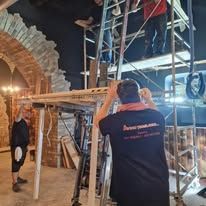 Operai che utilizzano impalcature e scale all'interno di un edificio con pareti in pietra in fase di costruzione.