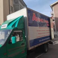 Camion delle consegne verde parcheggiato tra gli edifici, con pannello frontale blu e bianco e logo rosso sul lato.