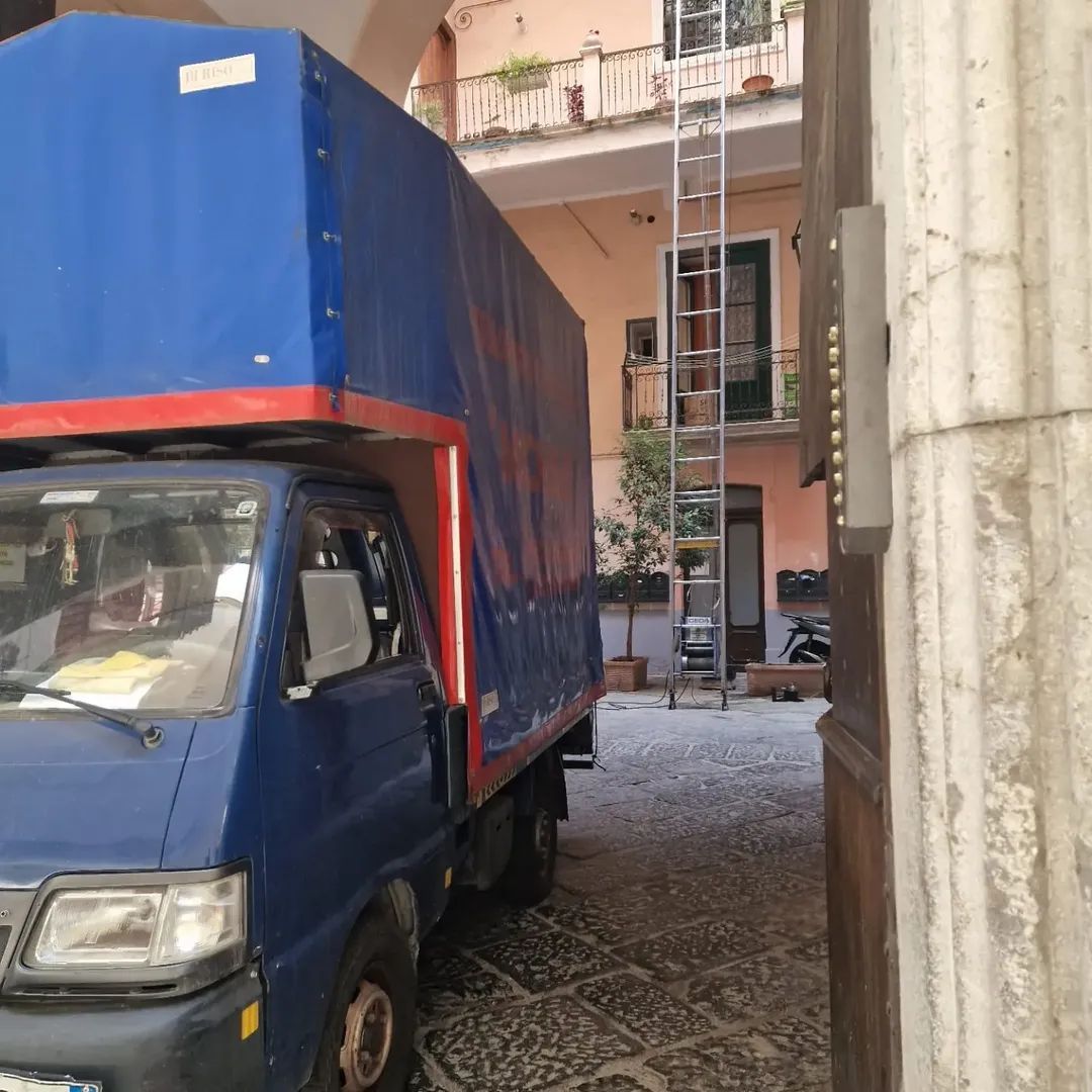 Camion blu da carico parcheggiato in uno stretto vicolo acciottolato accanto agli edifici.