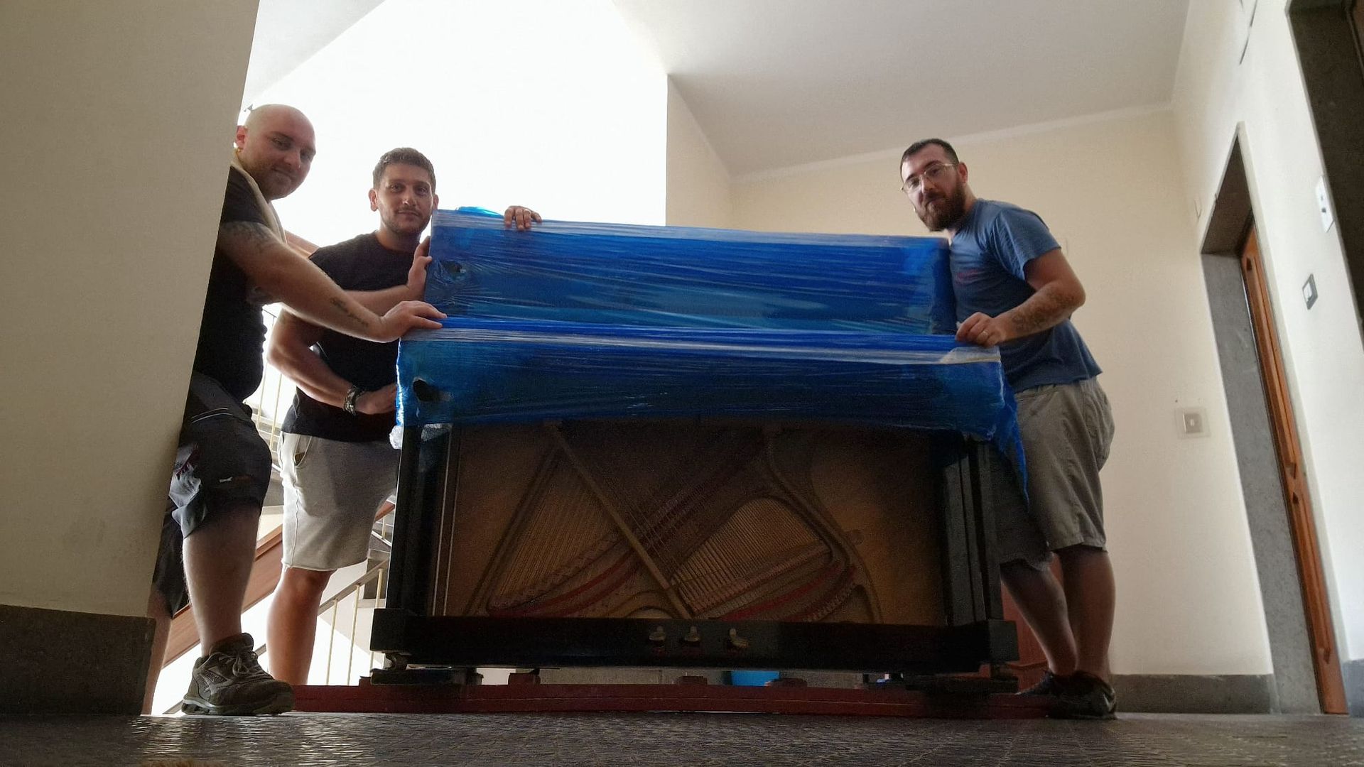 Tre traslocatori trasportano un pianoforte imballato su un carrello attraverso un corridoio