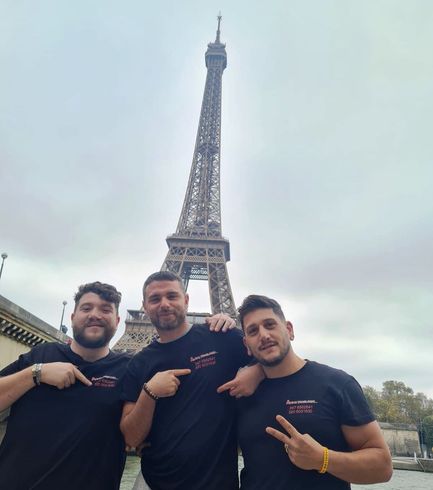 Tre persone in posa davanti alla Torre Eiffel, con indosso magliette nere, in una giornata nuvolosa.
