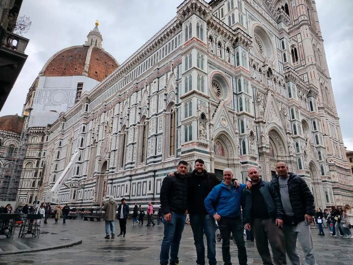 Cinque persone in posa davanti al Duomo di Firenze e al Campanile di Giotto in una piazza cittadina.