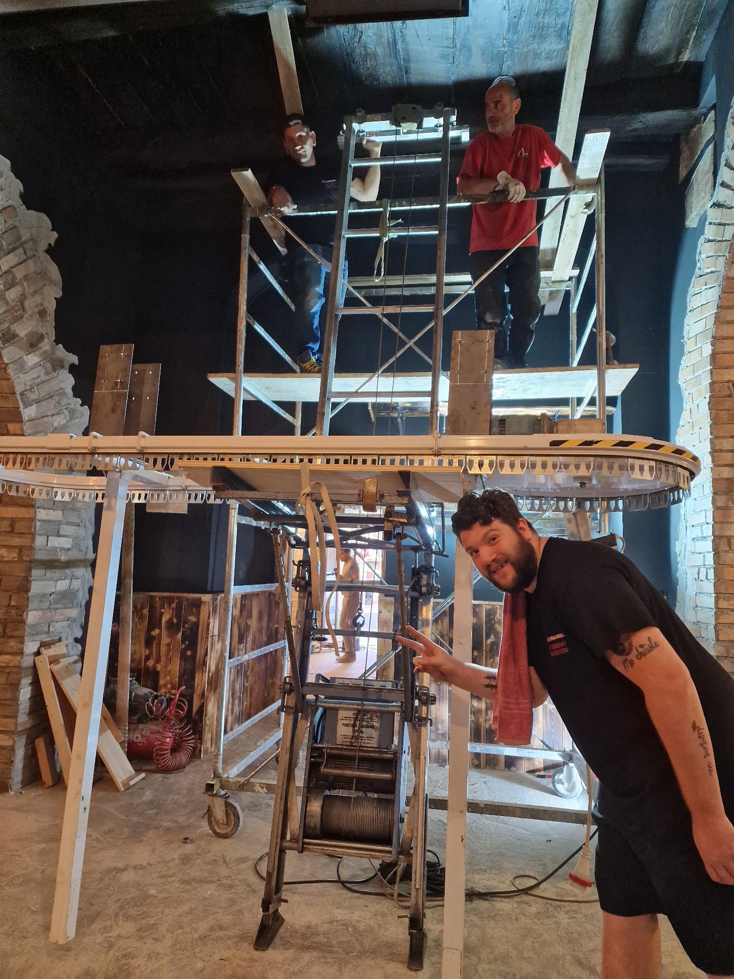 Operai su un'impalcatura in un cantiere edile, uno in rosso in alto e uno in nero in basso.