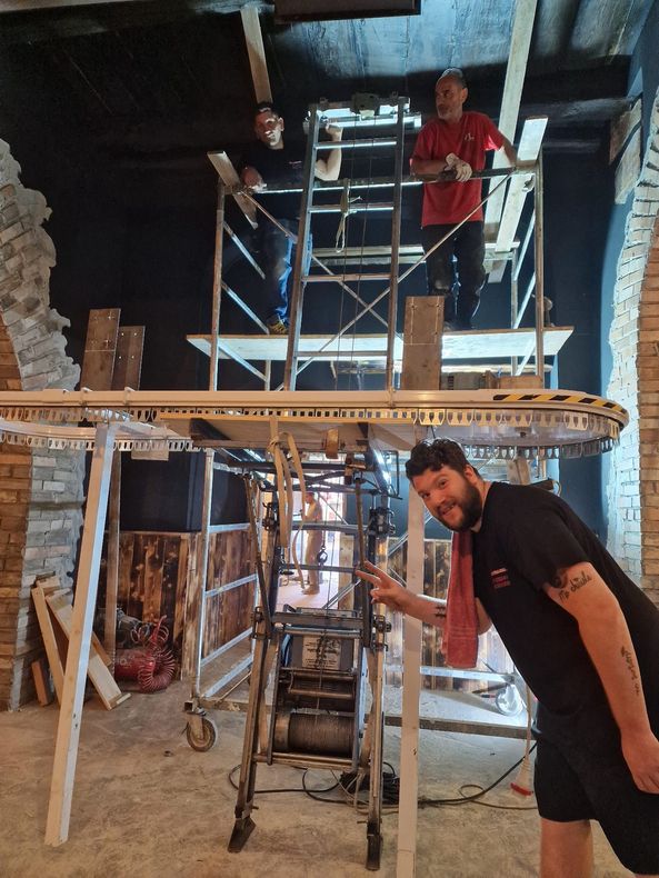 Operai su impalcature e scale in un cantiere edile al coperto e in penombra.