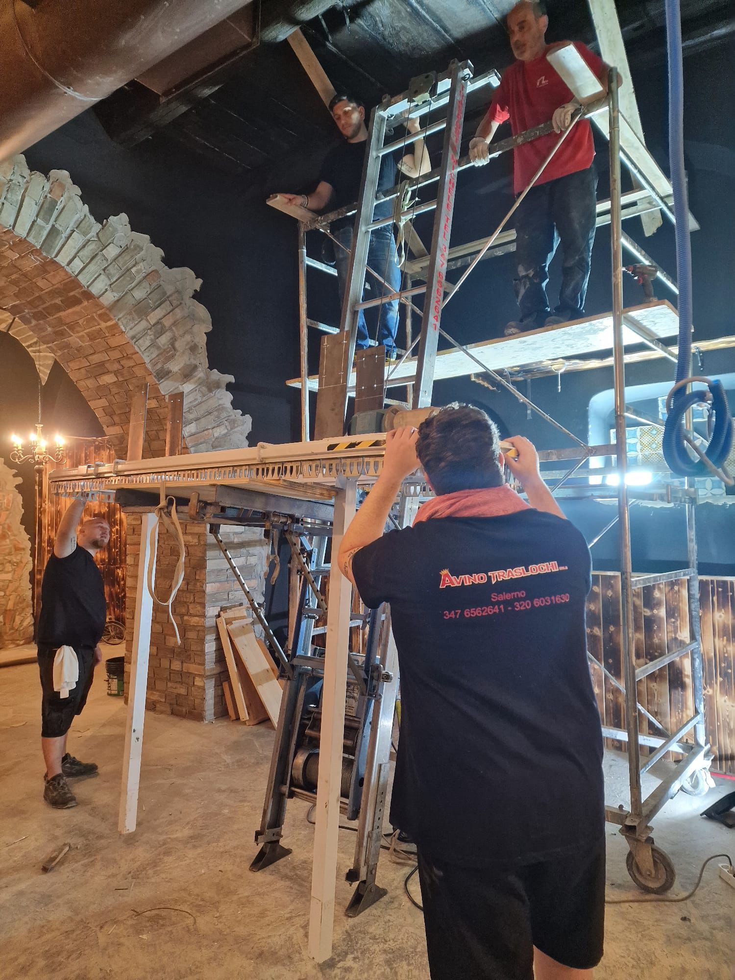 Operai su un'impalcatura e un uomo su una scala che riparano un arco in pietra all'interno