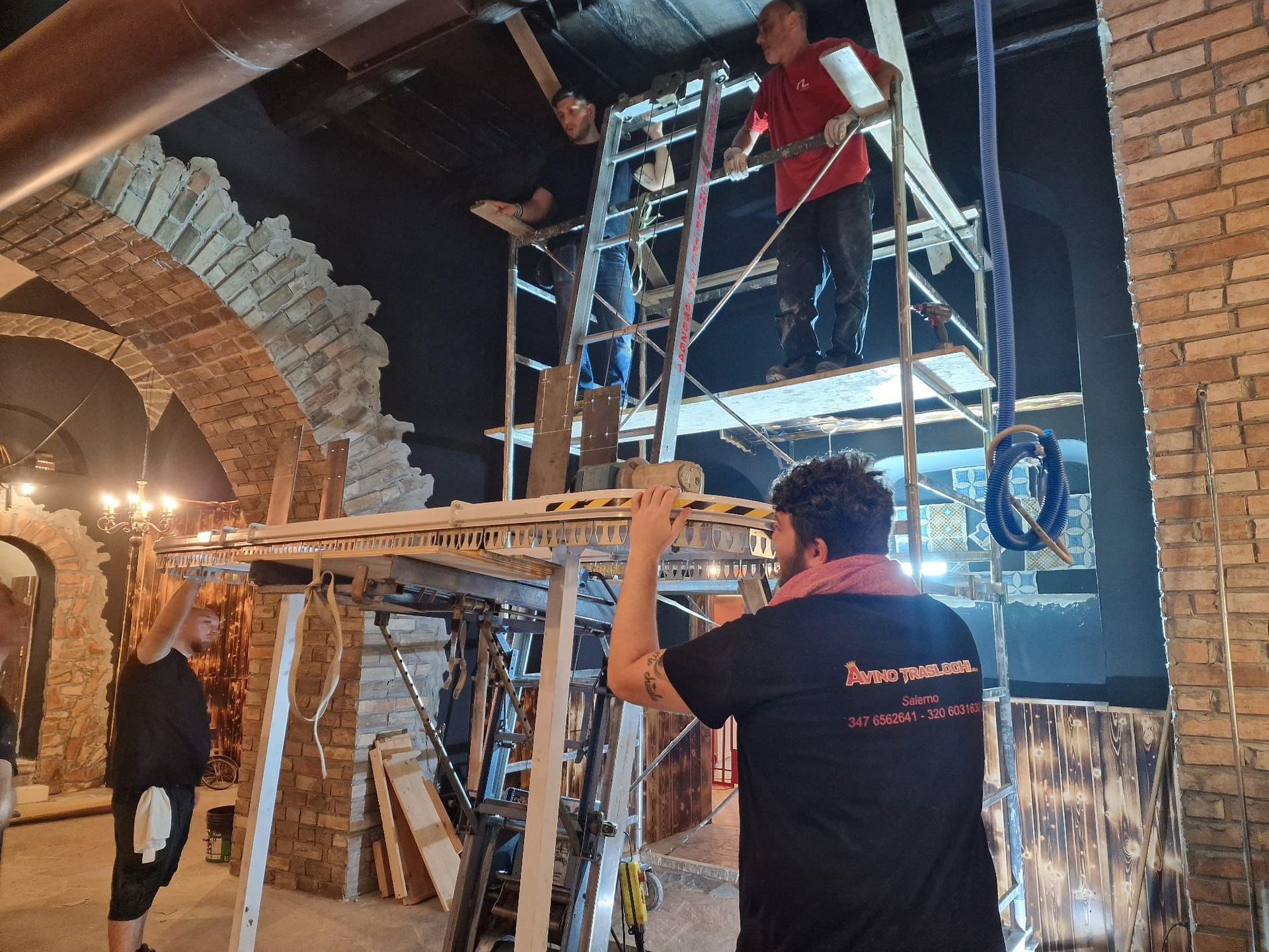 Operai intenti ad assemblare impalcature all'interno di un edificio in mattoni scarsamente illuminato.